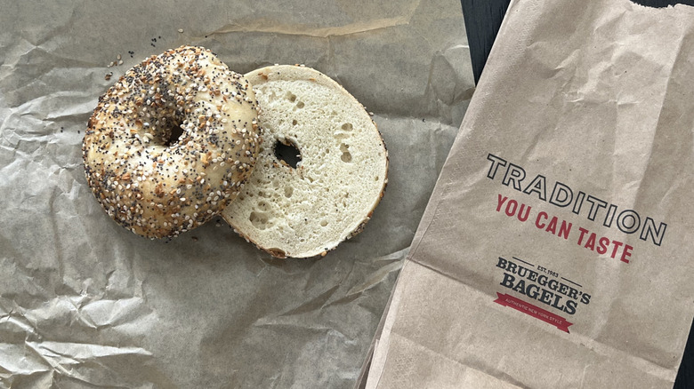 Bruegger's Bagels everything bagel sliced and placed on parchment paper with a to-go bag on the side