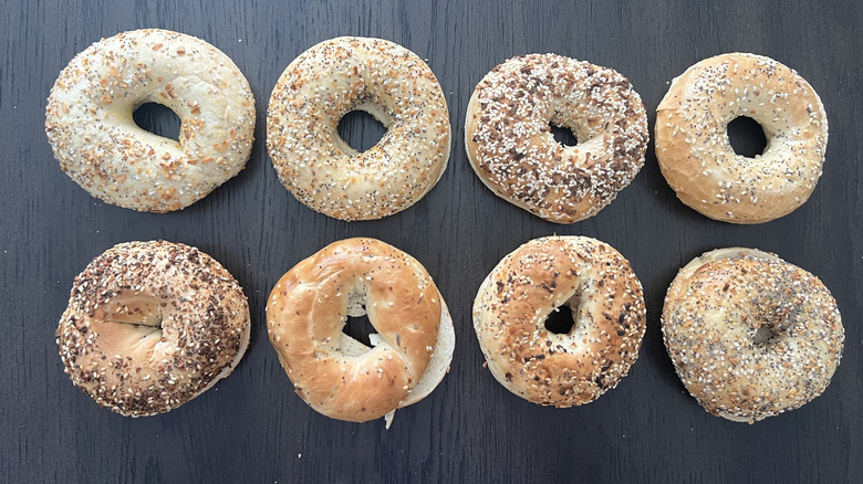 Everything bagels from 8 bakeries lined up on black wooden table