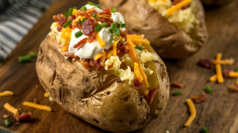A loaded baked potato sits on a wood board.
