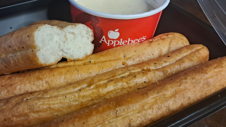 A portion of breadsticks next to a tub of Applebee's Alfredo sauce