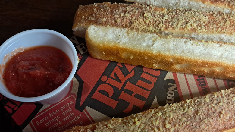 Pizza Hut breadsticks next to a tub of marinara sauce