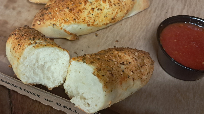 A halved breadstick with a pot of marinara sauce