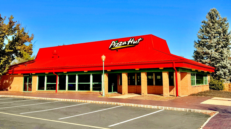 Pizza Hut restaurant with classic red roof in front of blue sky with empty parking lot
