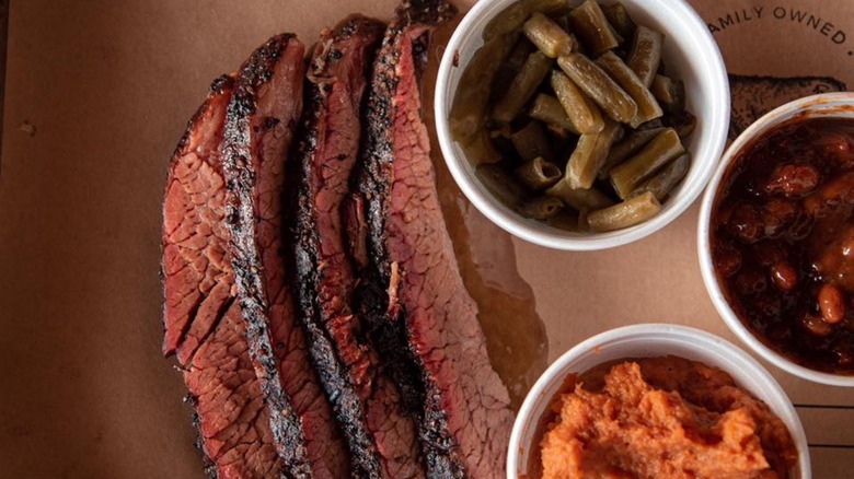 Slices of brisket with stryrofoam containers of beans on brown paper