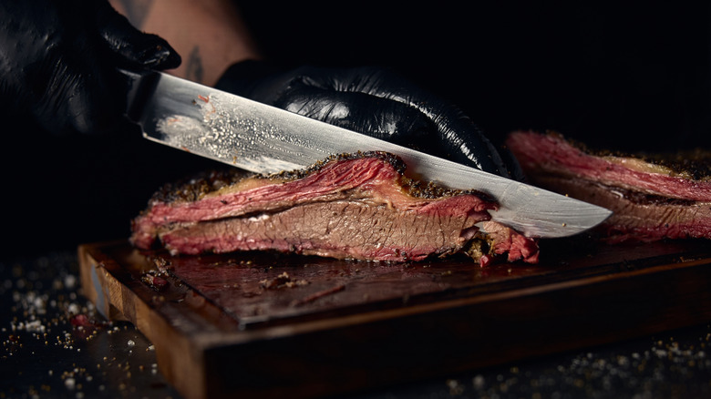 Hands wearing black gloves holding knife and slicing brisket