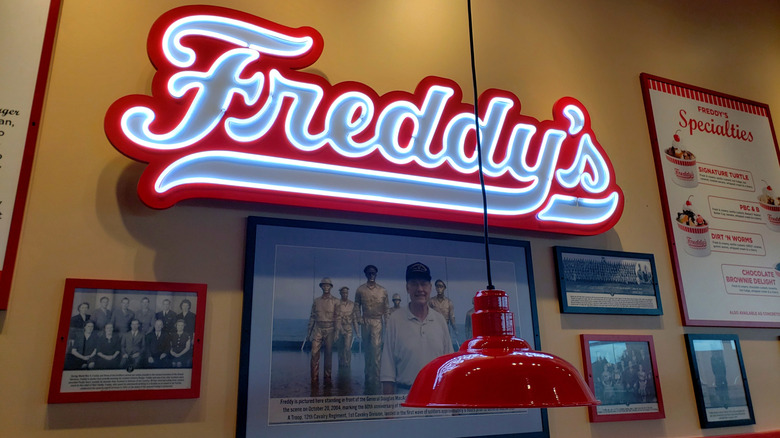 Decor inside of a Freddy's location featuring a neon sign, photos, and custard treats