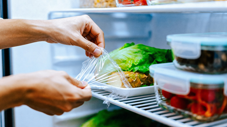 Person wrapping leftovers in the fridge