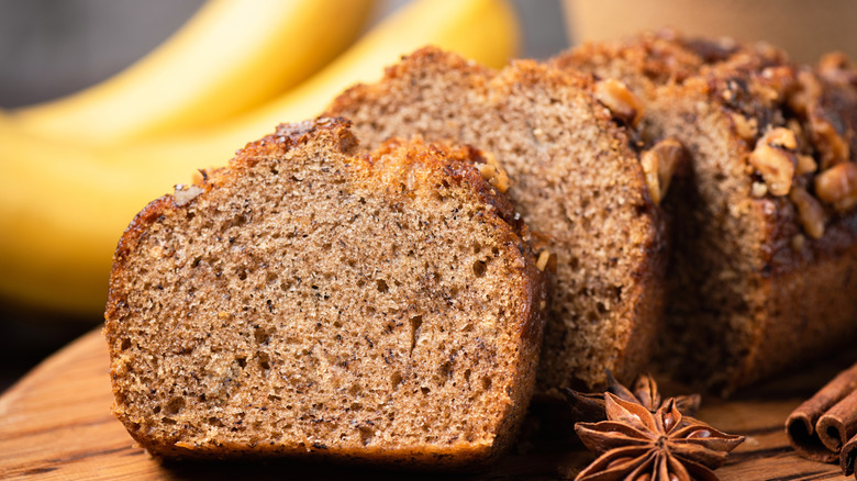 A sliced banana bread surrounded by bananas and cinnamon sticks