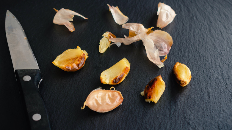 Overhead view of peeled roasted garlic cloves and a knife on a table