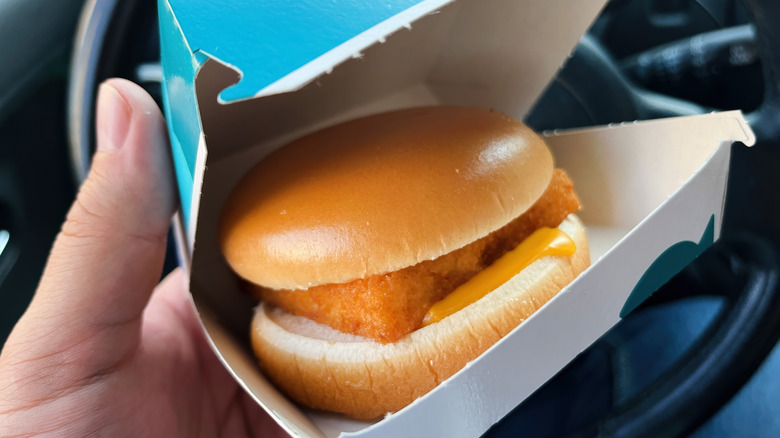 A close-up of a hand holding an open McDonald's Filet-O-Fish box inside a car