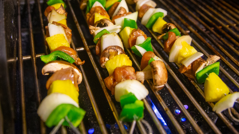 Vegetable and meat skewers on the grill over a blue flame