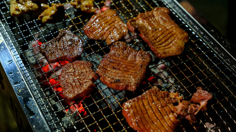 Cuts of beef grilling over charcoal