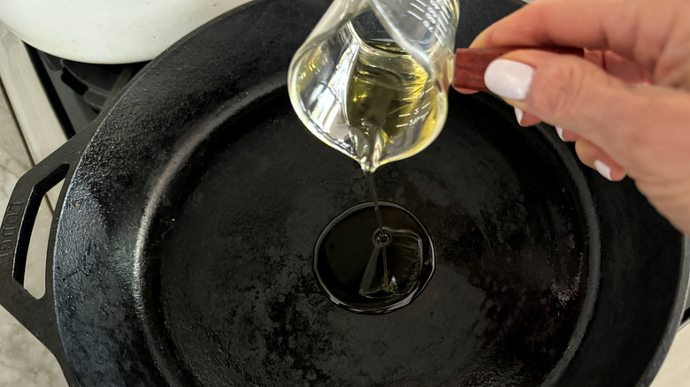hand adding oil to skillet