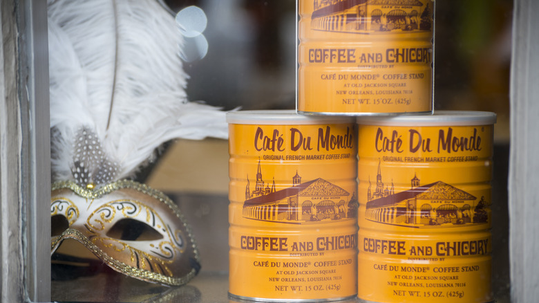 Café Du Monde coffee cannisters stacked in window next to Mardi Gras mask