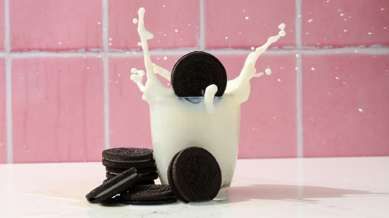 Oreo being dropped into a glass of milk, with several cookies next to the glass