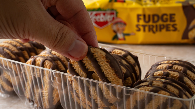 Hand picking up a Keebler Fudge Stripes cookie out of the plastic sleeve, with the outer packaging in the background