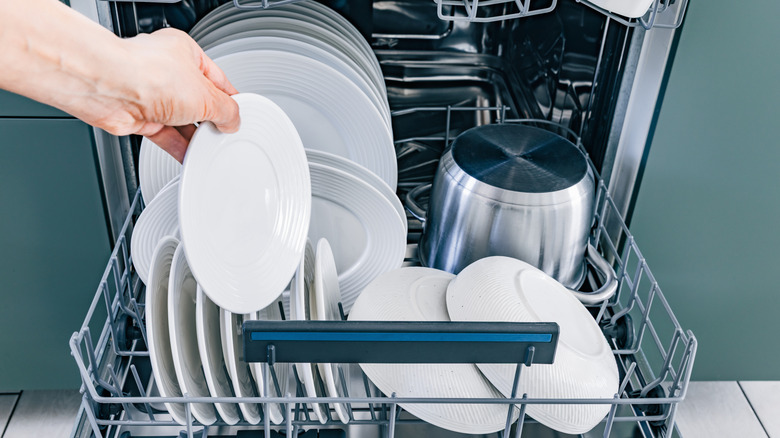 A person's hand loads a dish into a dishwasher.