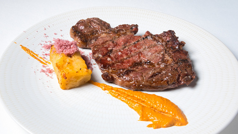 Artfully arranged plate with grilled beef, potatoes, and romesco sauce