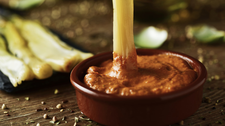 Roasted calcot onion being dipped in a ceramic dish of romesco sauce