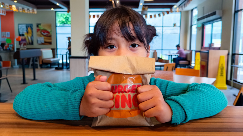A little girl holding a paper Burger King bag in front of her