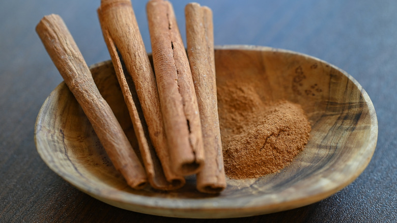 Dish of raw cinnamon powder and cinnamon sticks