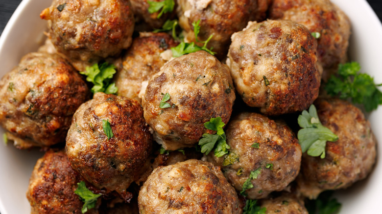 Close up on a bowl of cooked meatballs garnished with parsley