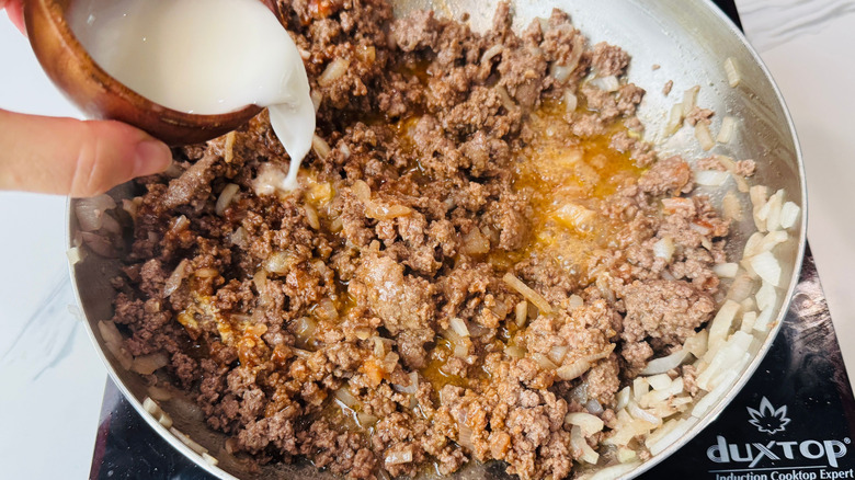Hand pouring cornstarch slurry into beef mixture
