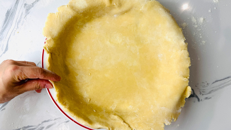 Hand pressing edge of pie crust in pie plate