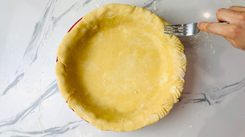 Hand pressing fork into pie crust to crimp edges