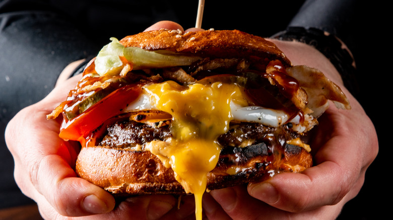 A drippy, messy cheeseburger being held in someone's hands