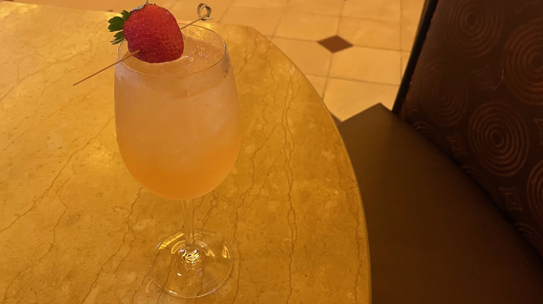 A Cheesecake Factory Peach Bellini Spritz sits on a table next to a brown booth.