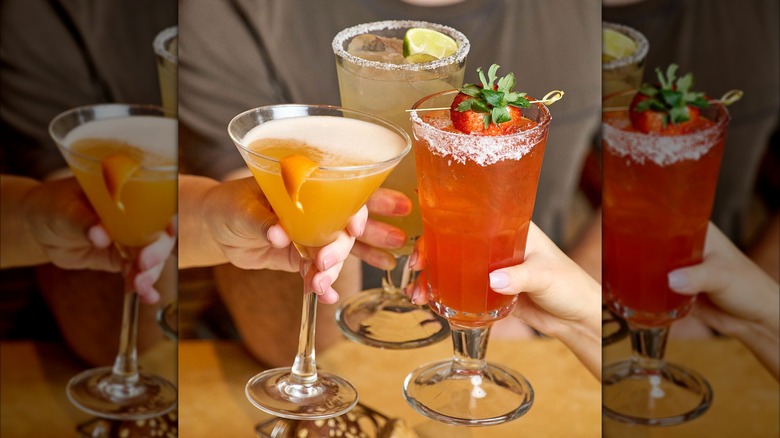 Three people clinking glasses of Cheesecake Factory cocktails including margarita with orange, strawberry cocktail, and plain margarita
