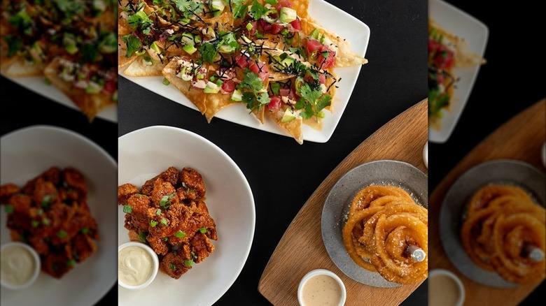 Yard House appetizers on black table including poke nachos, boneless wings, and onion ring tower
