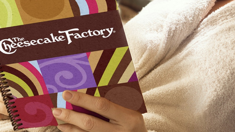 Cheesecake Factory menu held by person