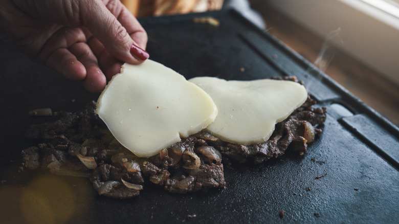 Woman putting cheese on top of cheesesteak meat on the grill