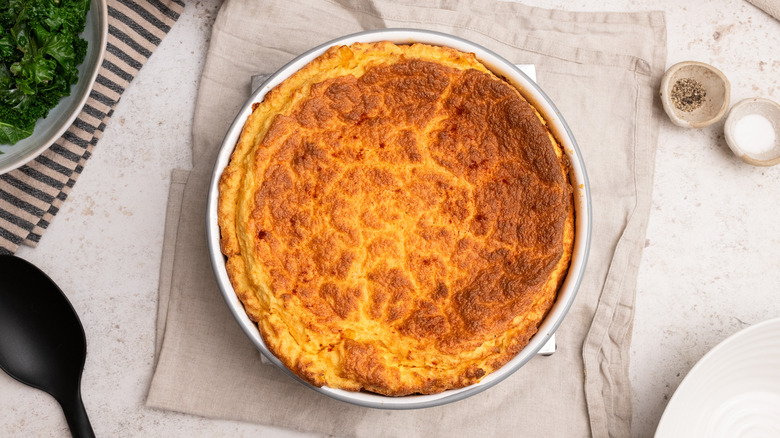 aerial view of cheesy corn souffle on cloth next to seasonings in small bowls