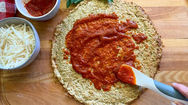 Easy gluten-free cauliflower pizza crust with sauce next to a bowl of cheese