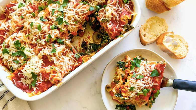 Kale lasagna in a white baking dish, with a piece being dished onto a plate