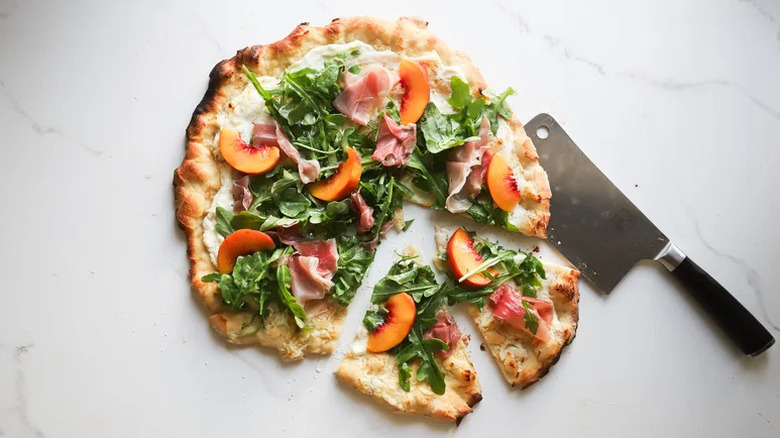 Arugula pizza with nectarines on a white marble countertop
