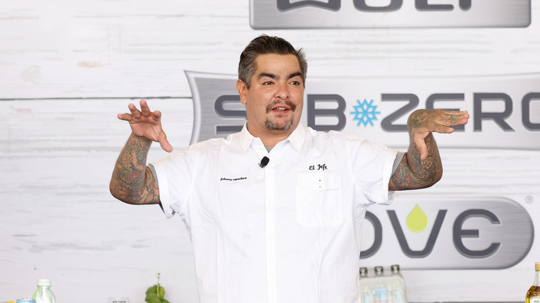 Chef Aarón Sánchez in a white chef's jacket with his arms raised