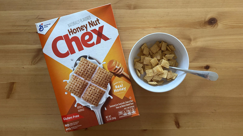 Box of Honey Nut Chex cereals with some cereals in a white bowl on wooden table