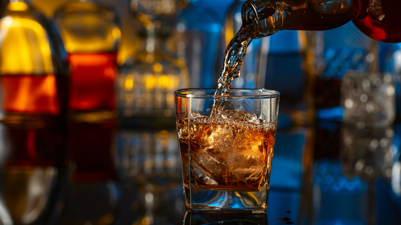 A glass of bourbon on ice being poured on a bartop