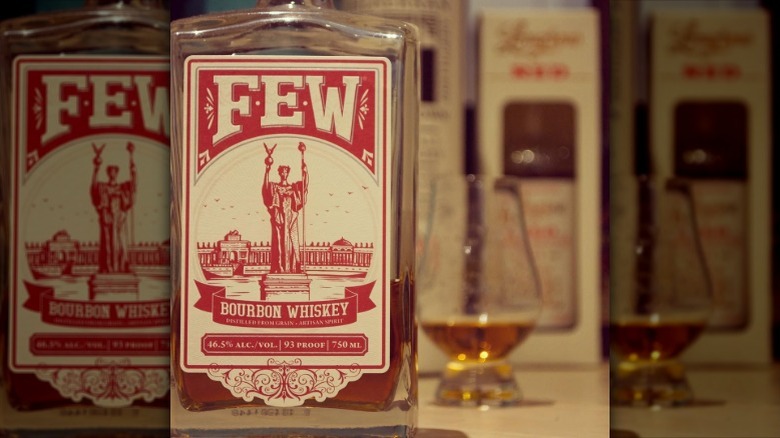 A close-up of the label of a bottle of Few bourbon whiskey, with a whiskey glass in the background