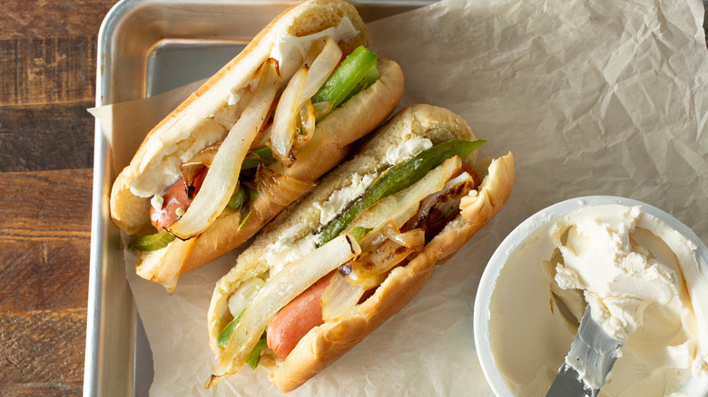 Seattle style hot dogs next to tub of cream cheese which is spread on the bun