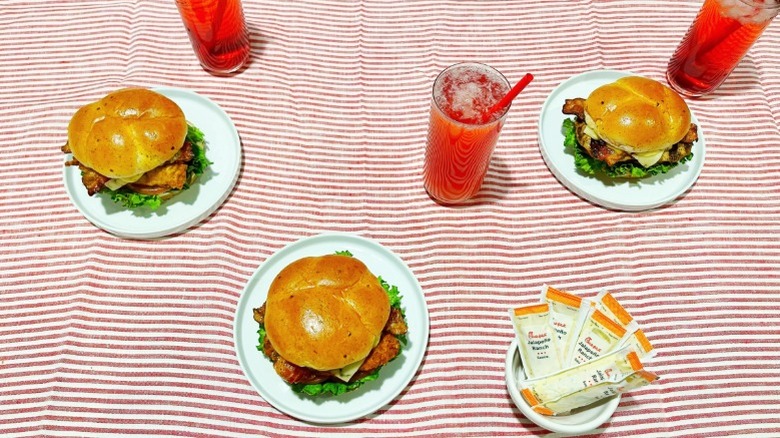 Three of Chick-fil-A's new sandwiches arrange over a striped tablecloth with strawberry hibiscus drinks