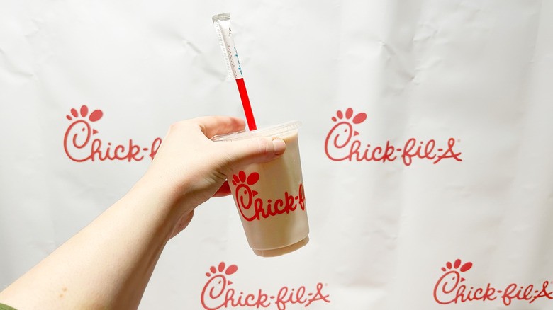 The strawberry hibiscus Frosted lemonade held by a hand in front of a Chick-fil-A backdrop