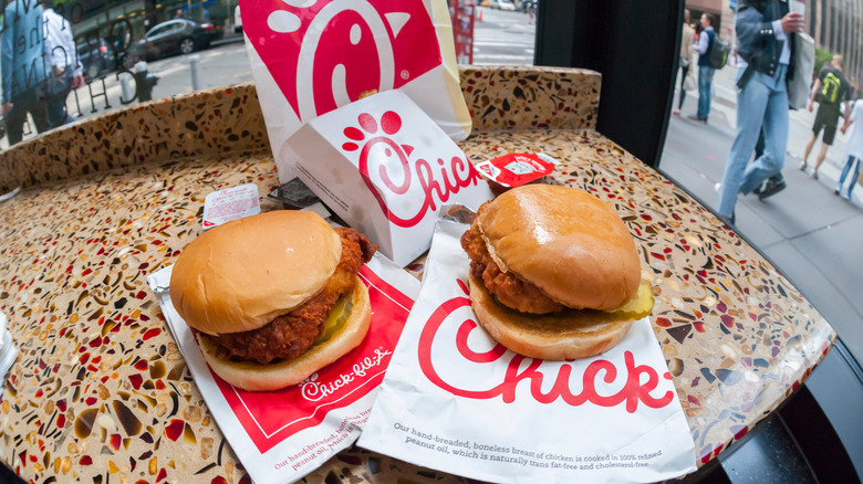 Two Chick-fil-A sandwiches sit side-by-side on a countertop with other branded bags