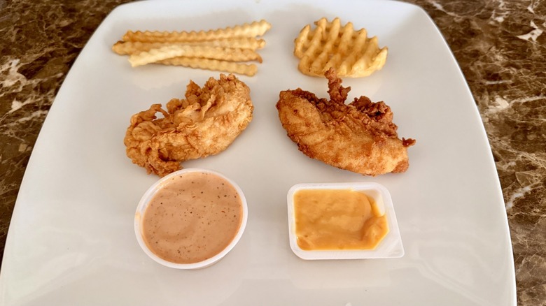 chicken tenders and fries on a white plate with dipping sauces
