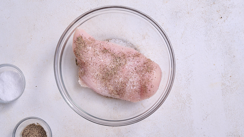 Chicken breast in bowl seasoned with salt and pepper