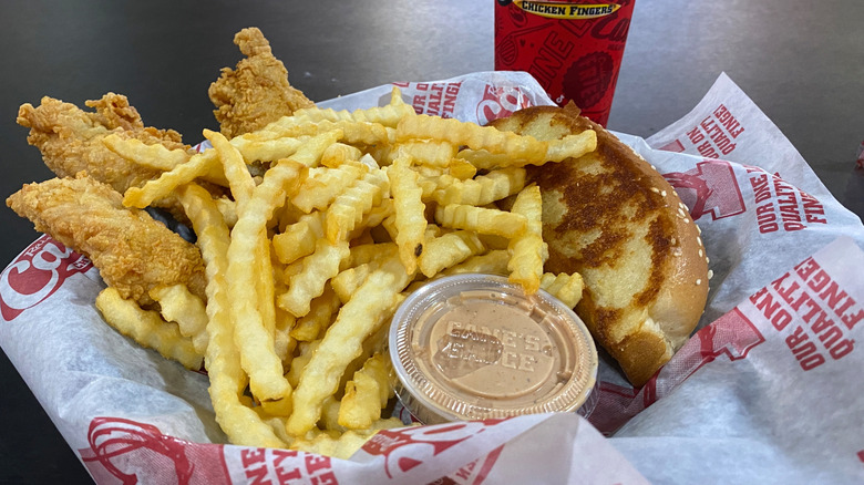 Raising Cane's chicken fingers and fries are in a basket with sauce.